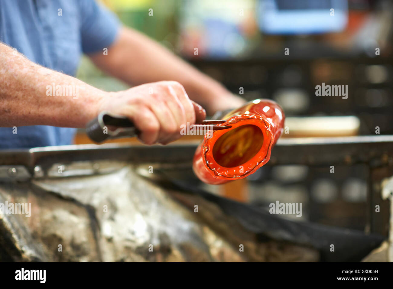 Glassblower in workshop shaping molten glass material with hand tools Stock Photo