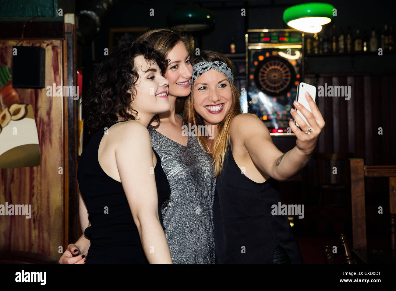 Three adult female friends taking smartphone selfie on night out in bar Stock Photo