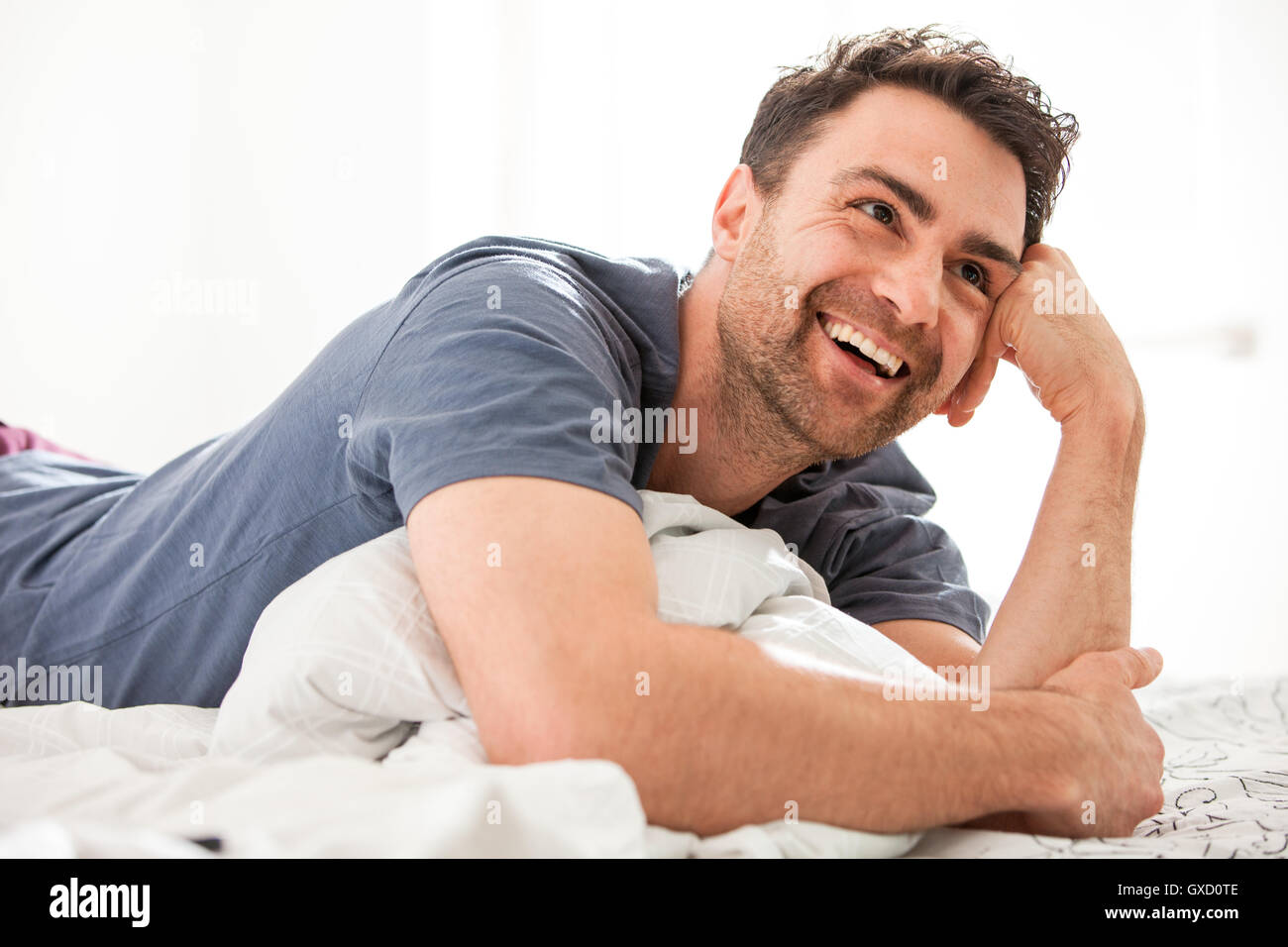 Man lying on bed, resting on elbow looking away smiling Stock Photo