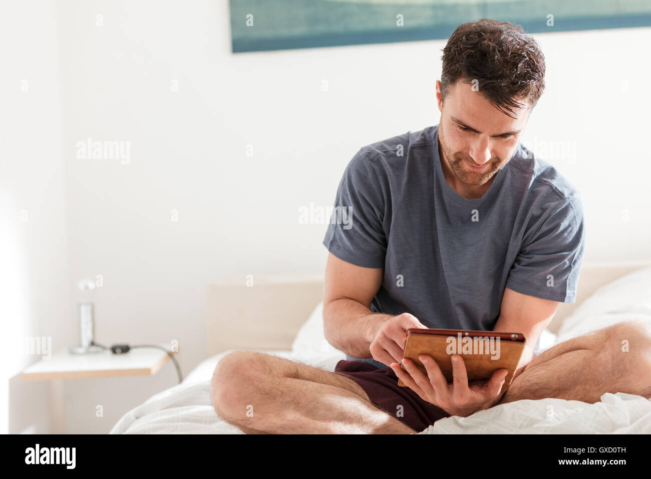Man sitting on bed using digital tablet Stock Photo