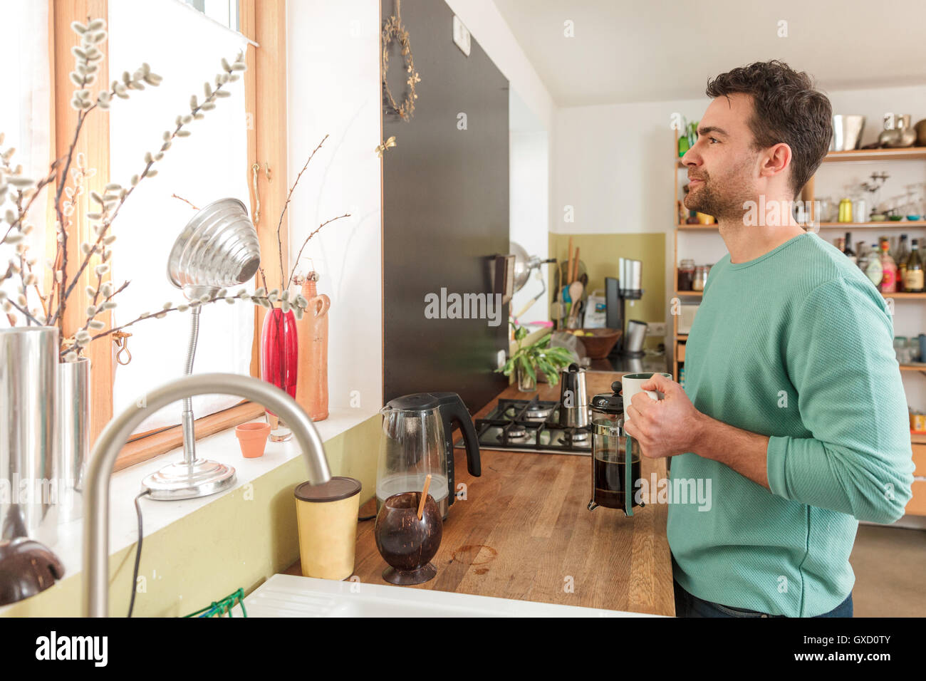 Man in kitchen holding coffee cup looking out of window Stock Photo