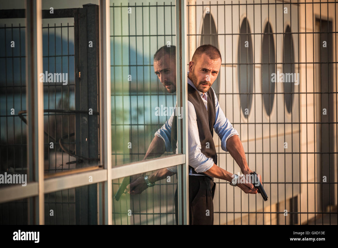 Man in business attire poised behind corner with handgun, Cagliari, Sardinia, Italy Stock Photo