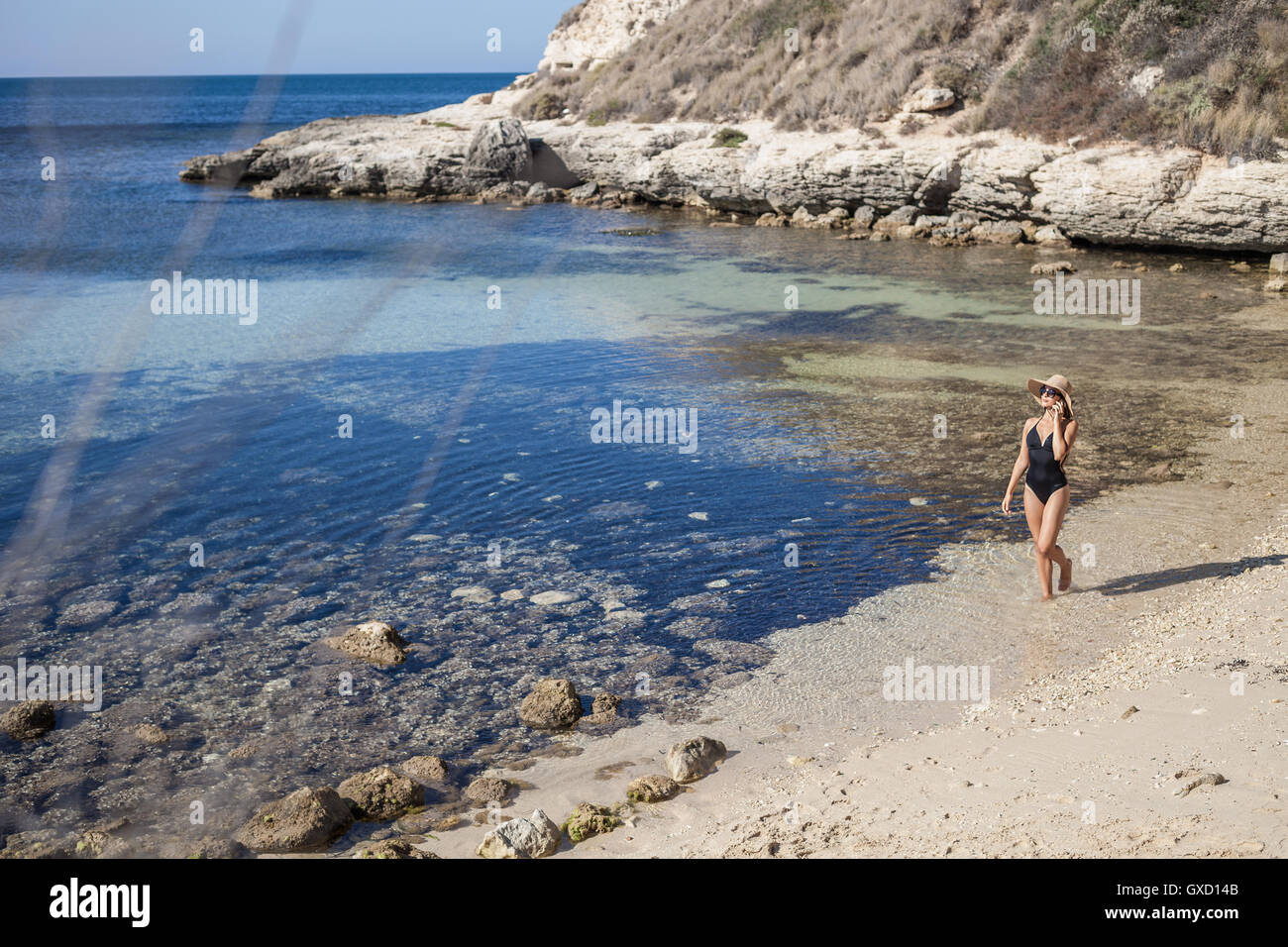 Young woman wearing swimming costume chatting on smartphone on beach, Villasimius, Sardinia, Italy Stock Photo