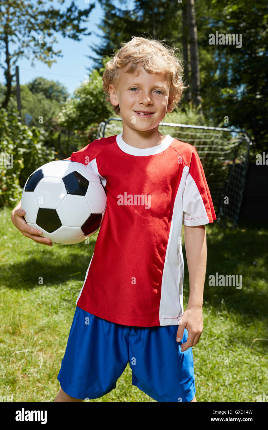 Portrait of boy wearing soccer uniform holding soccer ball in garden Stock Photo