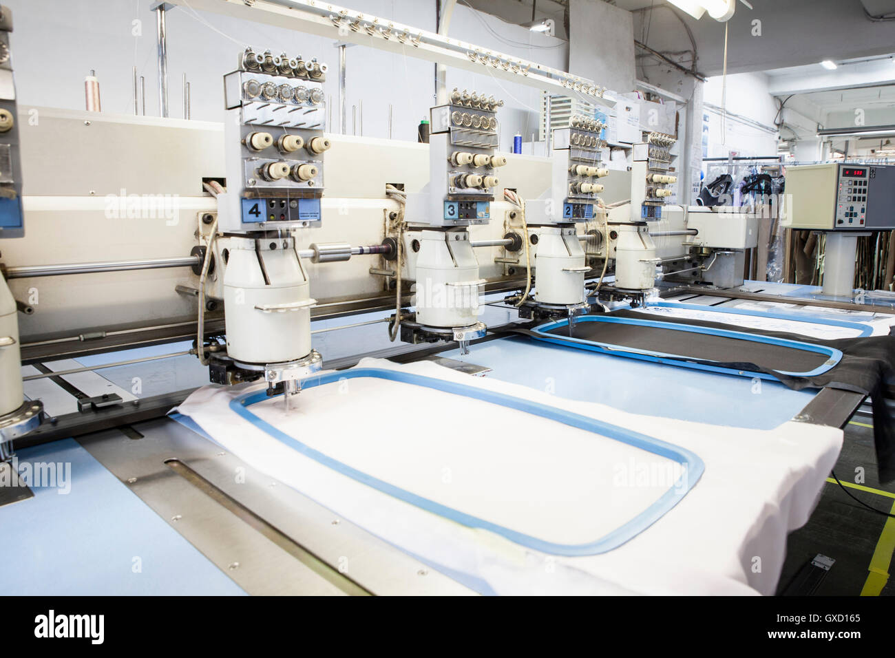 Rows of programmed embroidery machines speed stitching in clothing factory Stock Photo