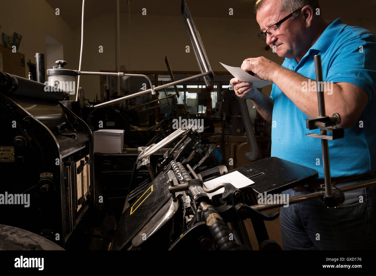 Mature male printer inspecting paper for printing machinery in printing press workshop Stock Photo
