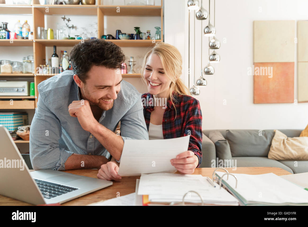 Couple with laptop looking at paperwork smiling Stock Photo