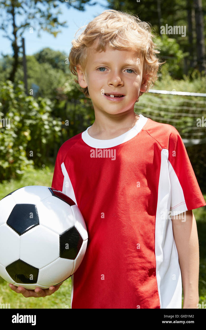 Close up portrait of boy wearing soccer uniform holding soccer ball in garden Stock Photo