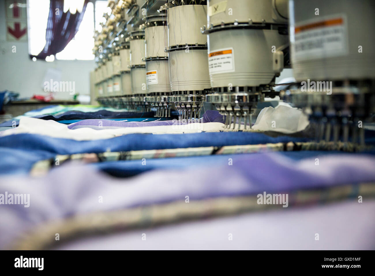 Rows of programmed embroidery machines speed stitching blue cloth in clothing factory Stock Photo
