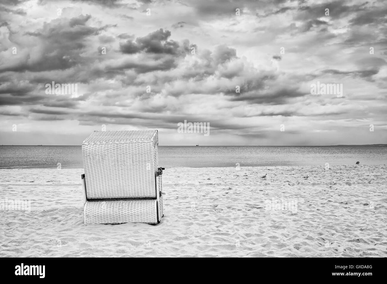 Hooded wicker basket chair on an empty beach, black and white filter applied. Stock Photo