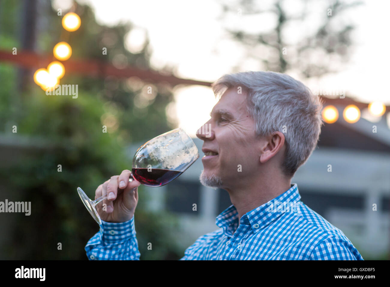 Mature man drinking red wine at garden party at dusk Stock Photo