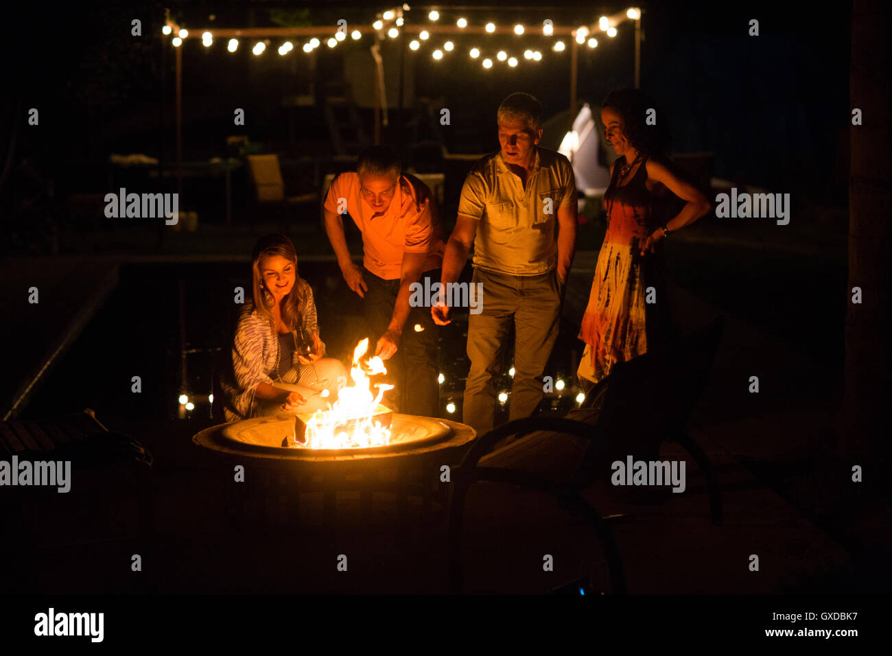 Mature adult couples  toasting marshmallows on patio fire at night Stock Photo