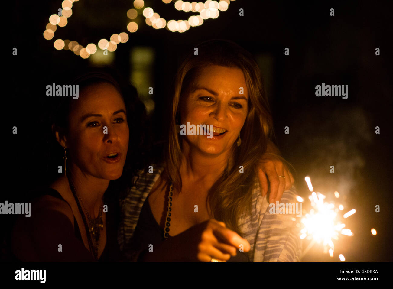 Mature female friends playing with sparkler in garden at night Stock Photo