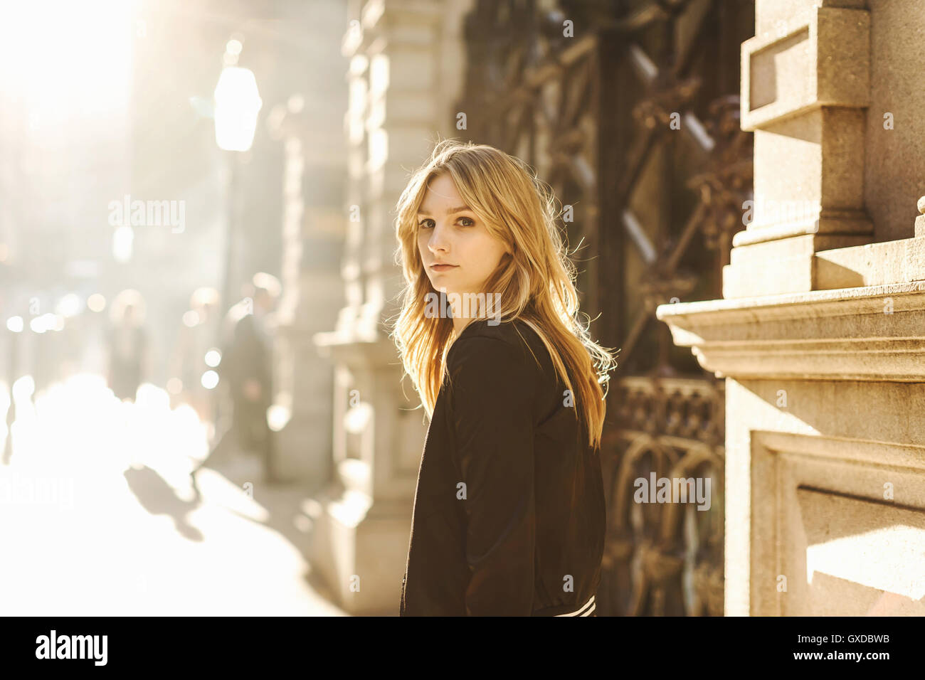 Young woman standing in street, looking over shoulder, pensive expression Stock Photo