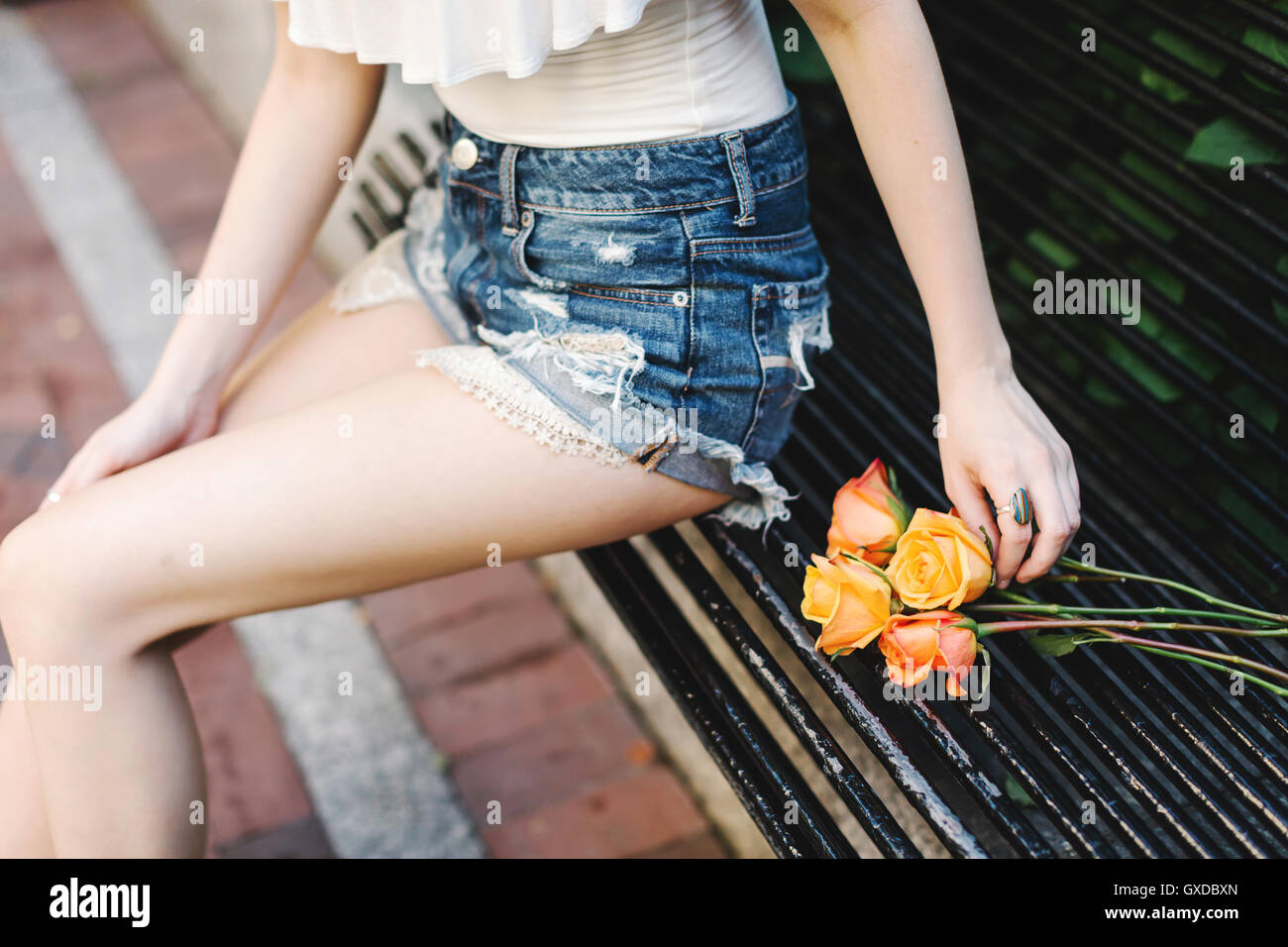 Young woman sitting on bench, roses beside her, mid section Stock Photo