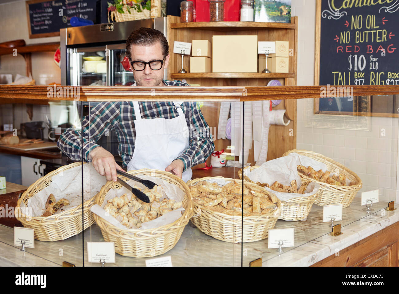 Male worker in bakery, taking fresh goods from basket Stock Photo