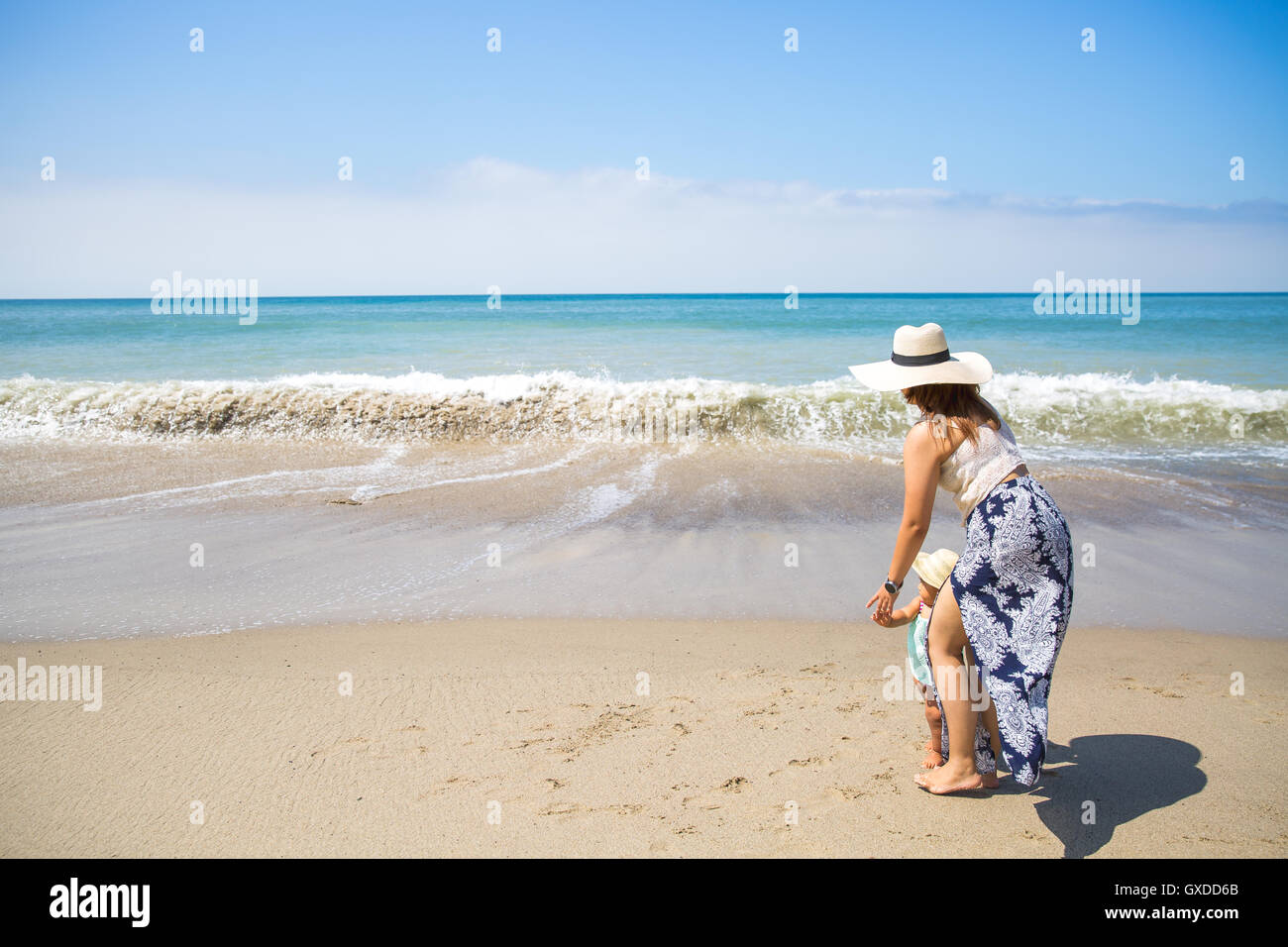 Mother holding hands with baby son on beach, Malibu, California, USA Stock Photo