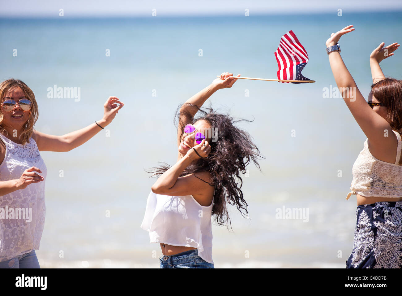 Three adult female friends waving American flag on beach, Malibu, California, USA Stock Photo