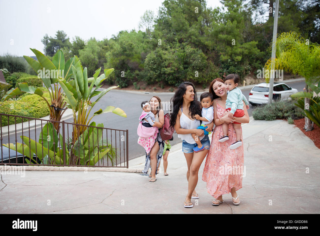 Women carrying baby daughter and sons moving up driveway, Malibu, California, USA Stock Photo