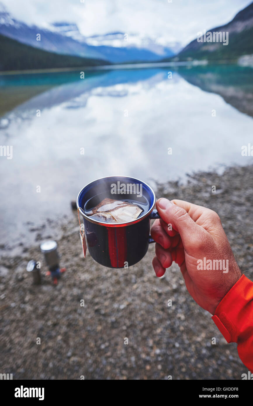Cropped view of mans hand holding cup of tea by river, Banff, Alberta, Canada Stock Photo