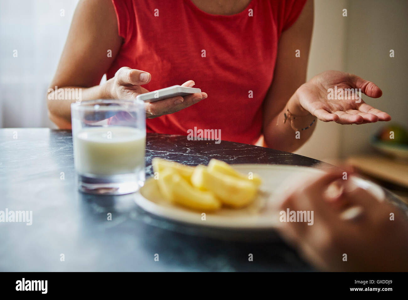 Cropped view of woman at dining table holding smartphone Stock Photo