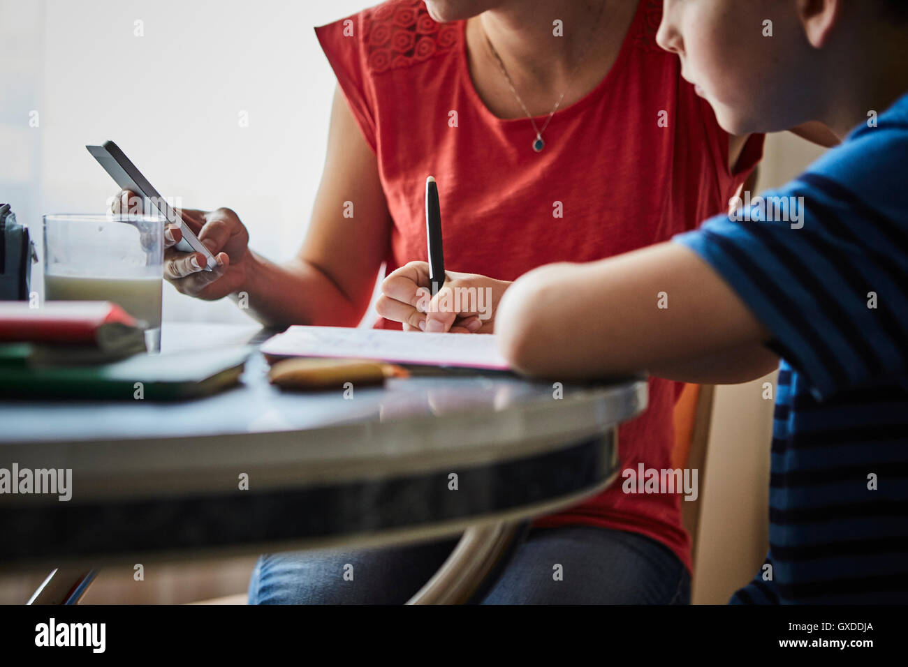 Mother at dining table helping son with homework Stock Photo