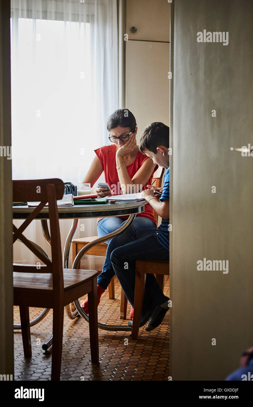 Mother at dining table helping son with homework Stock Photo