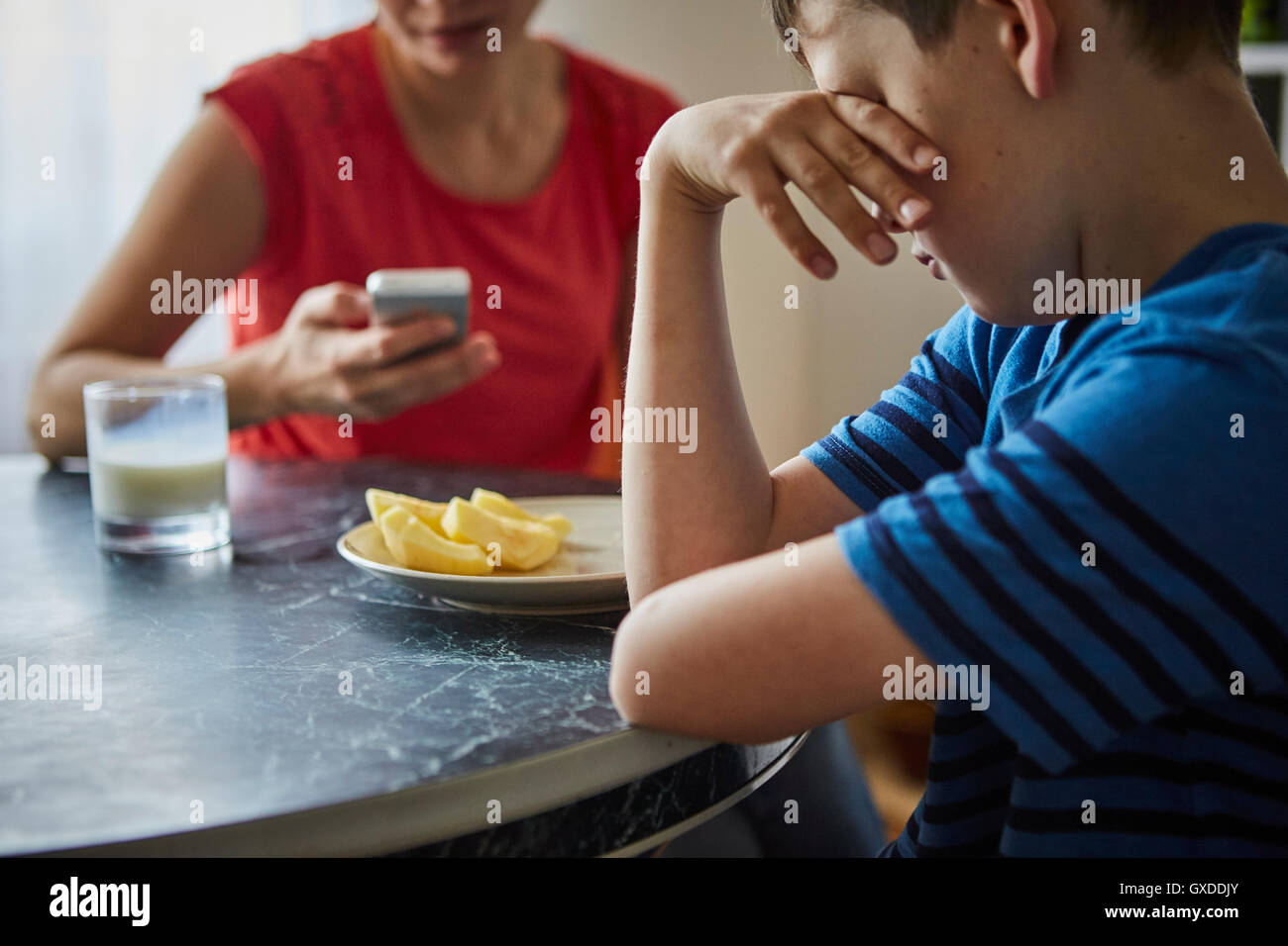 Boy at dining table, hand on eyes looking upset Stock Photo