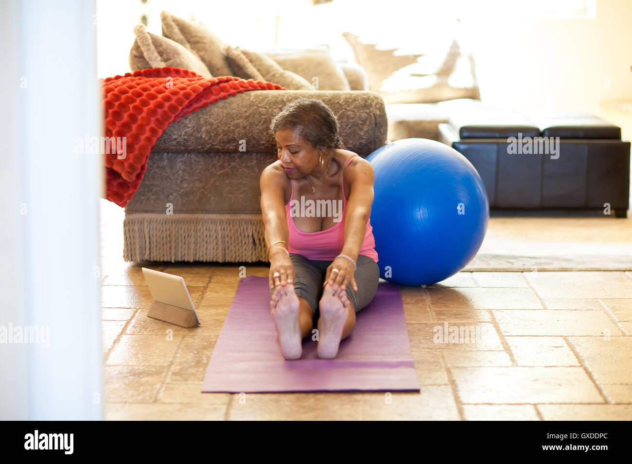 Woman on yoga mat using digital tablet, stretching Stock Photo