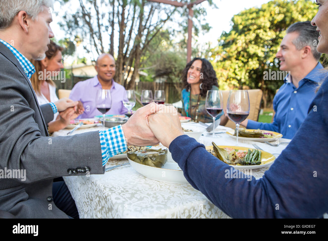 Six mature adult friends holding each others hands at garden party table Stock Photo