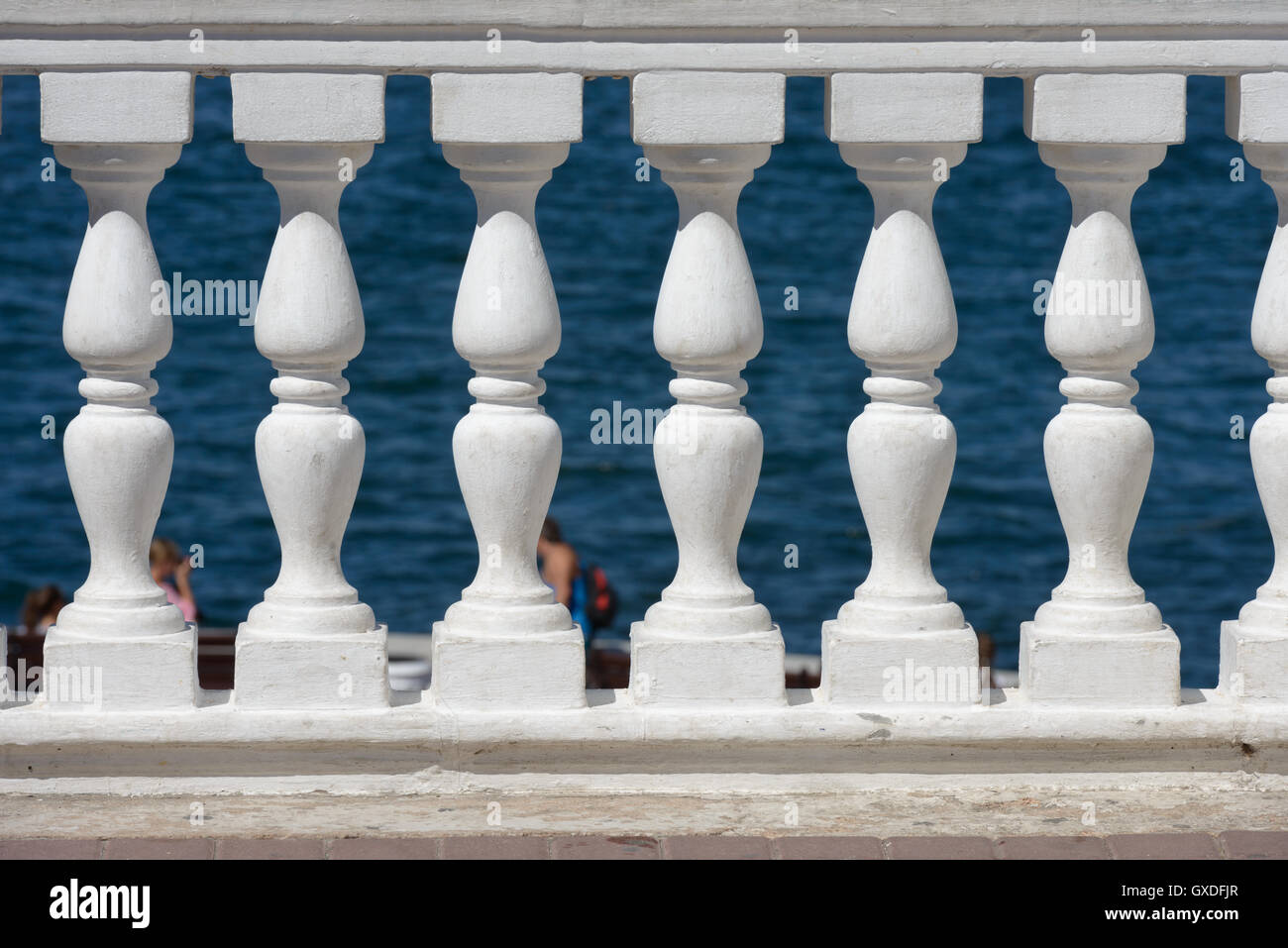 Old concrete balustrade painted white on blue sea background Stock