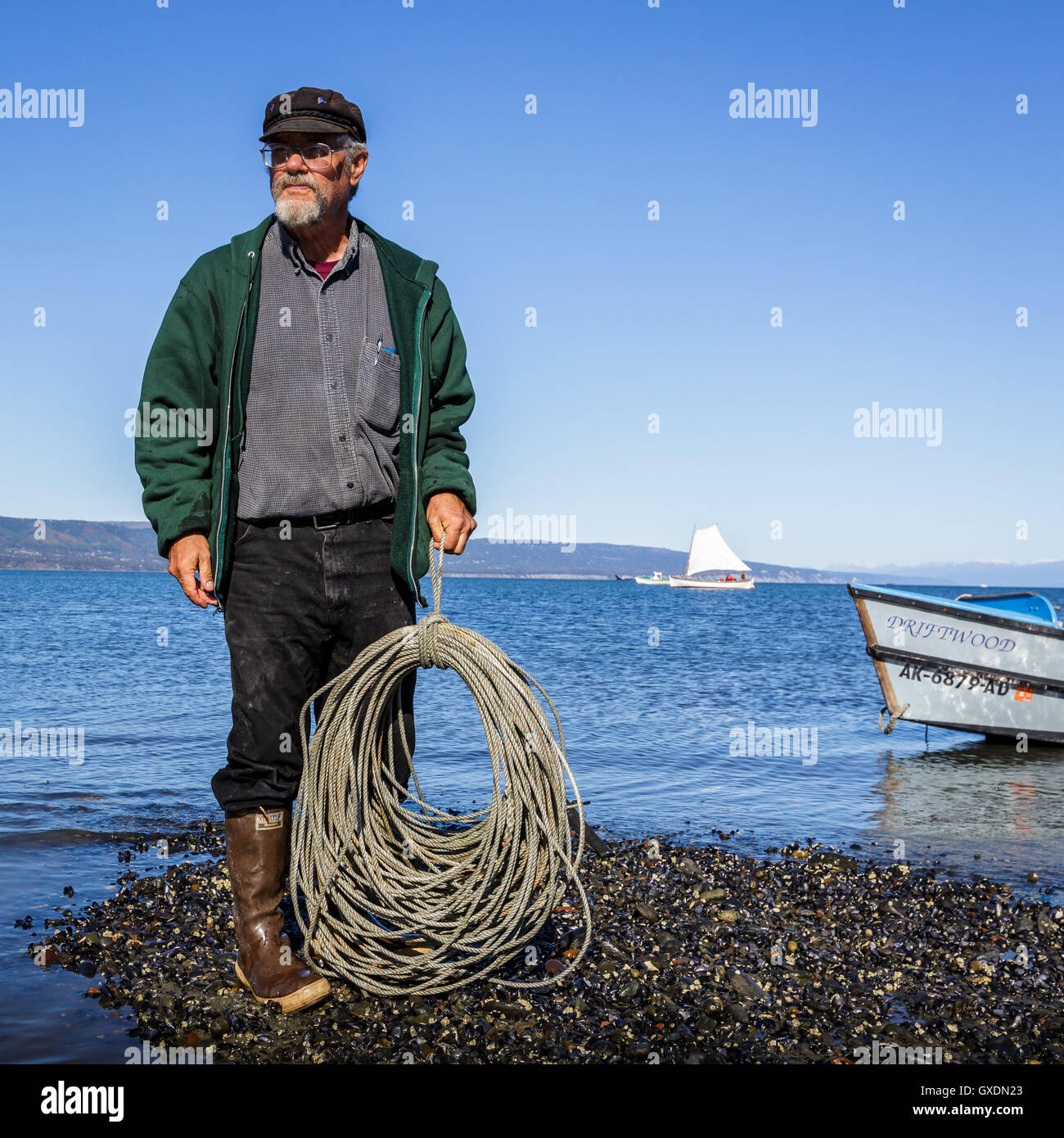 https://c8.alamy.com/comp/GXDN23/a-man-stands-on-the-beach-next-to-the-sea-holding-a-coil-of-rope-held-GXDN23.jpg