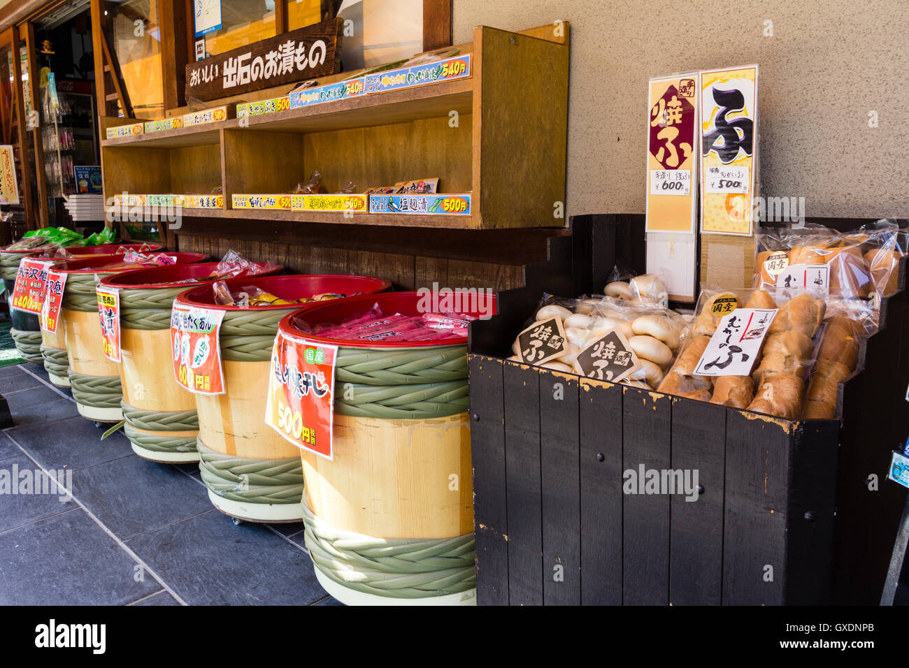Japan, Izushi. Row of four tubs and packets of tourist souvenir sweets and foods in barrels arranged on pavement outside store. Stock Photo