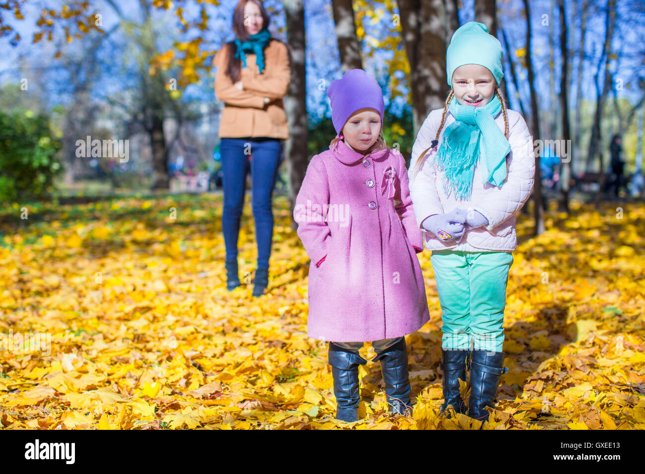 Two adorable girls with his young mom in the park on a sunny autumn day ...
