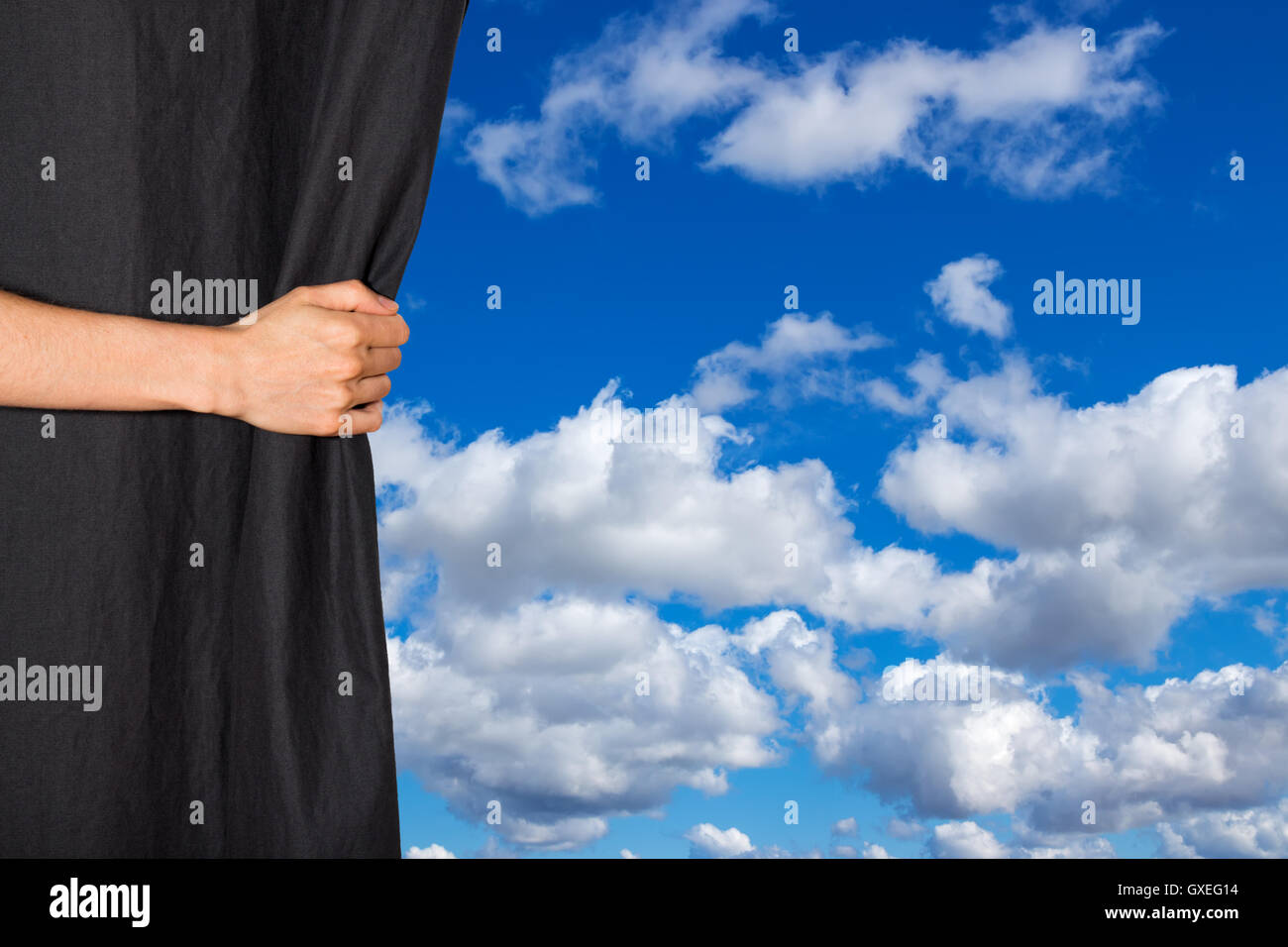 Hand opening black curtain with sky behind it Stock Photo