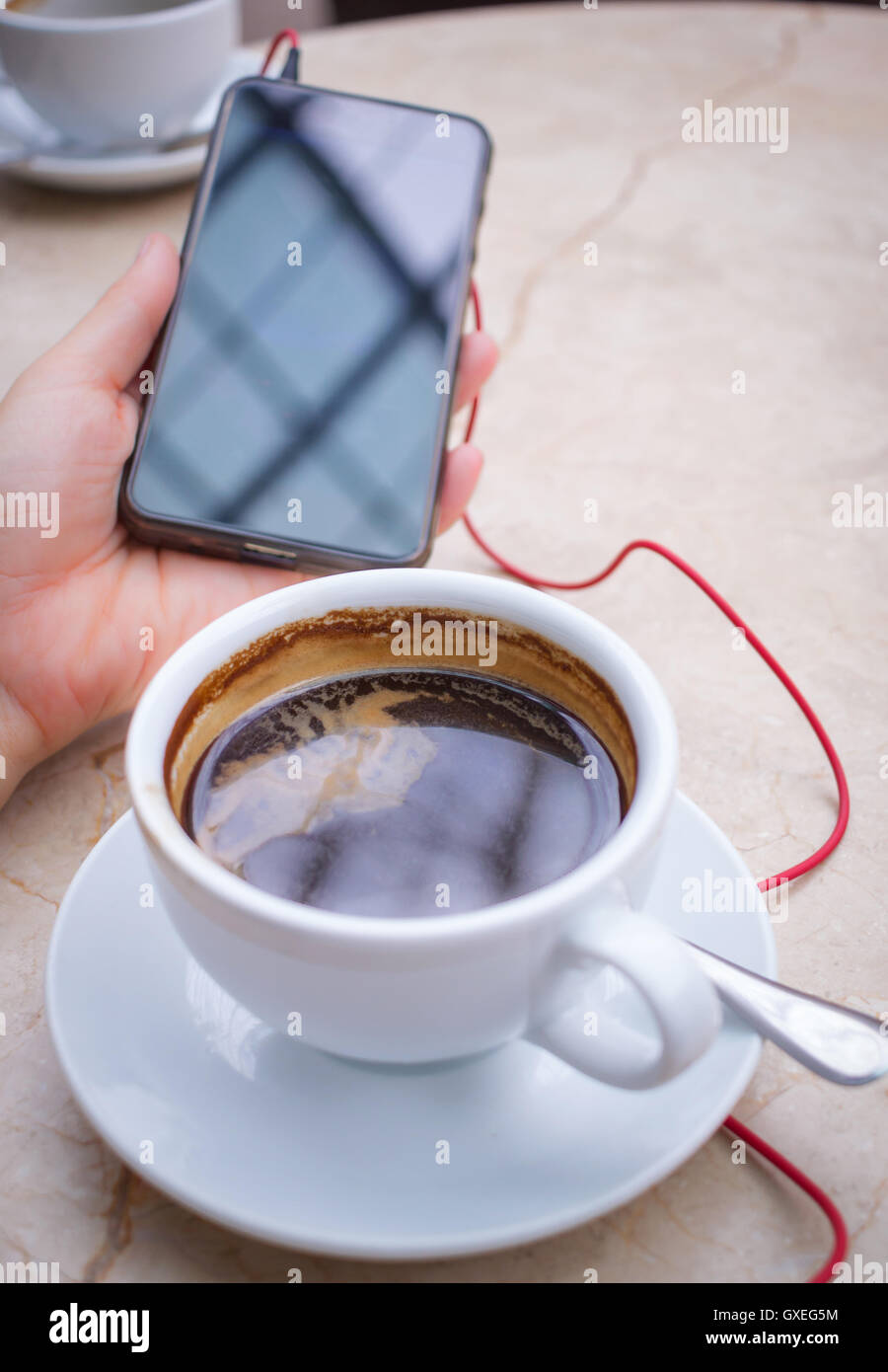 Smartphone at hand and americano coffee in white cup at marble table top Stock Photo