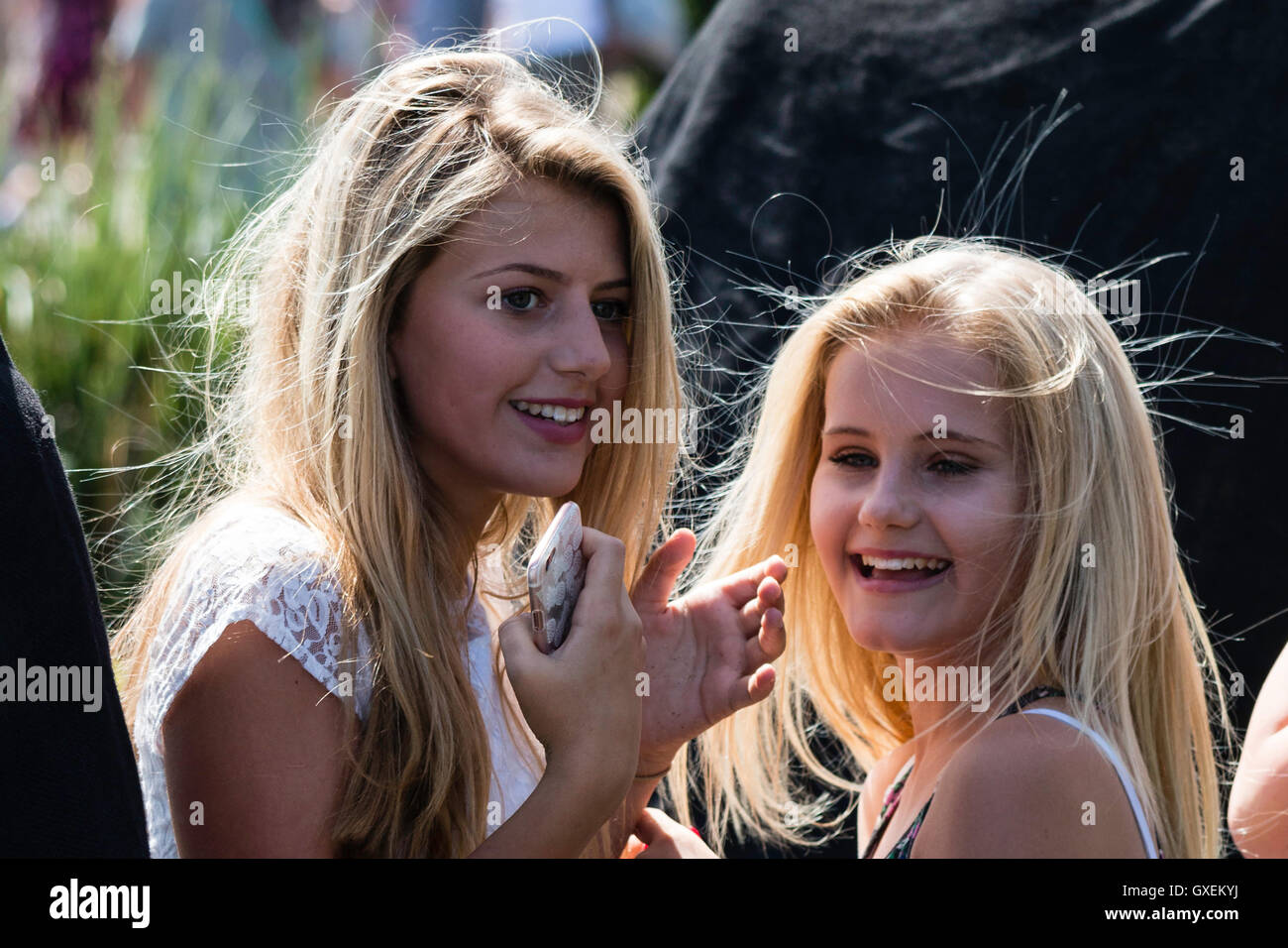 Two blonde teenage girls, 13-14 years old, both turned their heads to face while laughing, sunlight catching their hair. Head shot. No eye-contact. Stock Photo