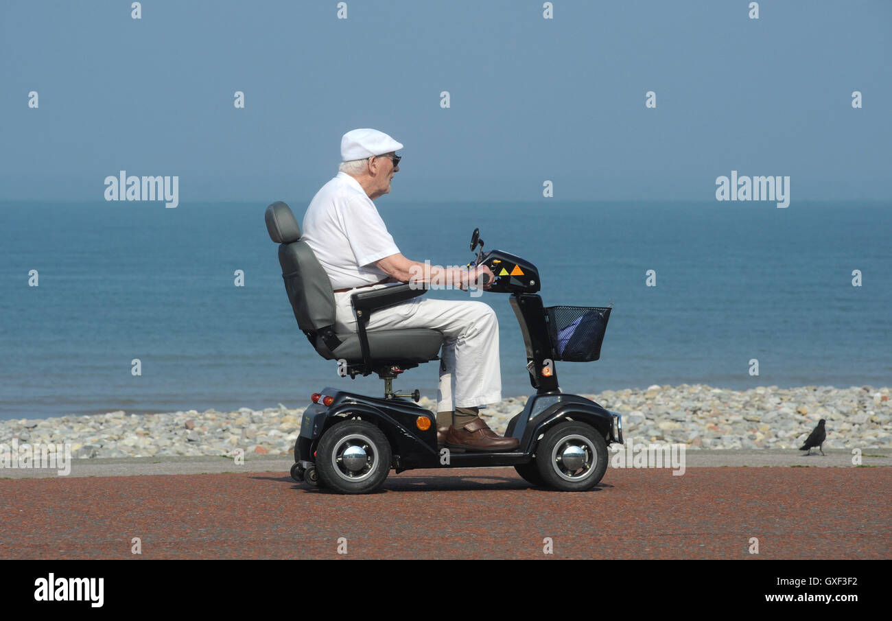 ELDERLY MAN RIDING DISABILITY SCOOTER ON COASTAL PROMENADE RE DISABLED