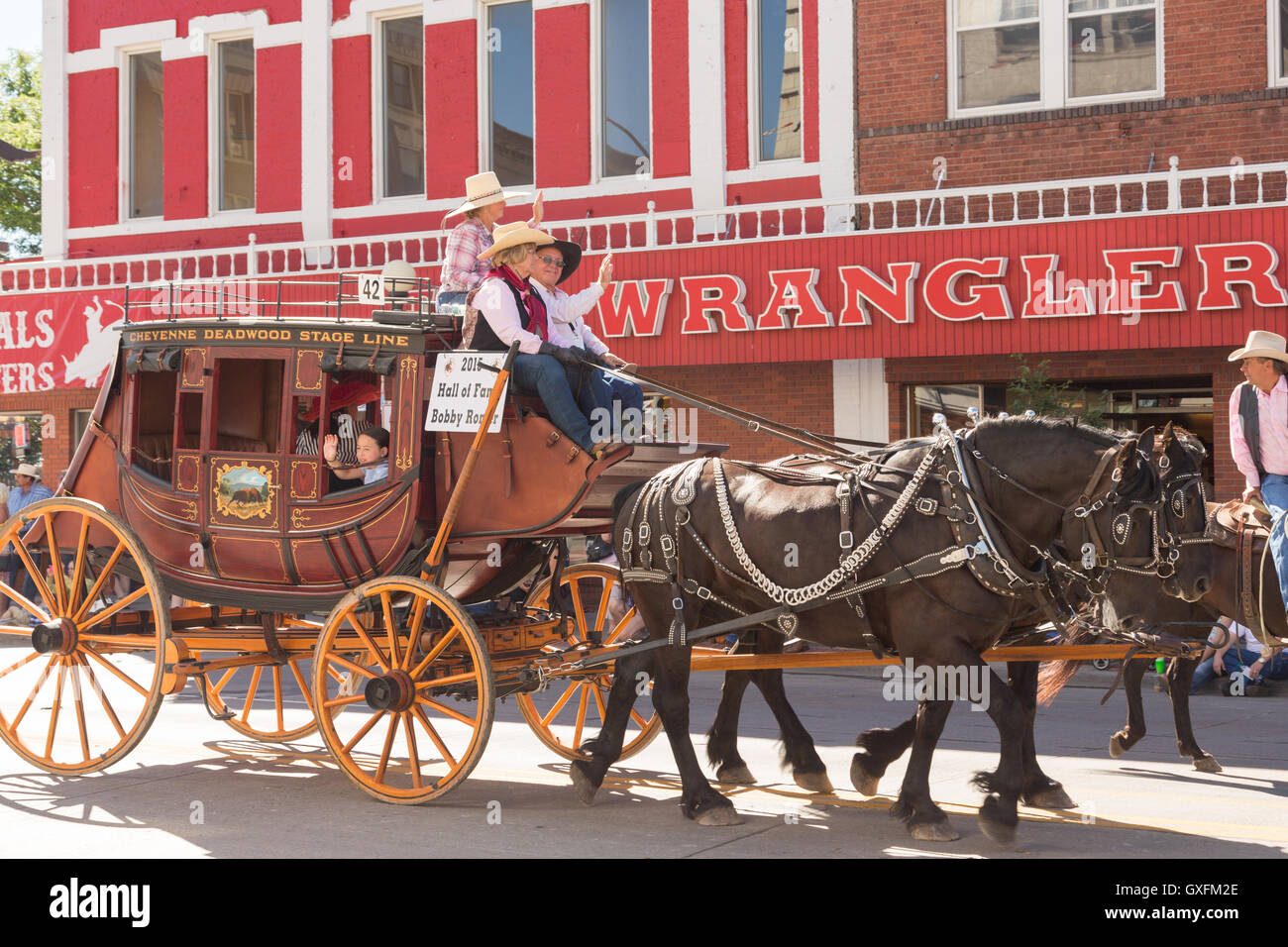 A stagecoach wagon pasts the Wrangler western wear store during the Cheyenne Frontier Days parade through the state capital July 23, 2015 in Cheyenne, Wyoming. Frontier Days celebrates the cowboy traditions of the west with a rodeo, parade and fair. Stock Photo