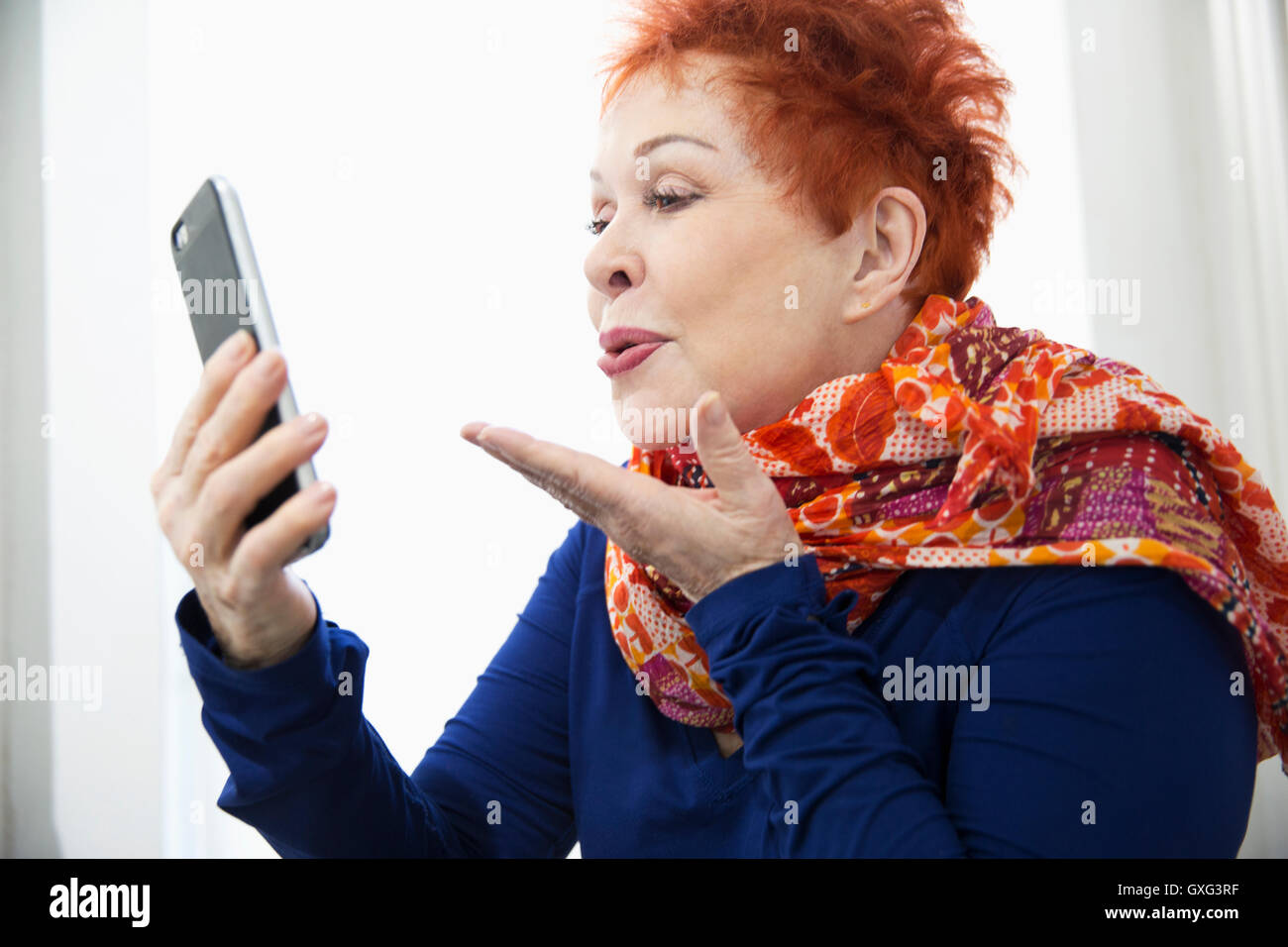 Older Caucasian woman blowing kiss at cell phone Stock Photo