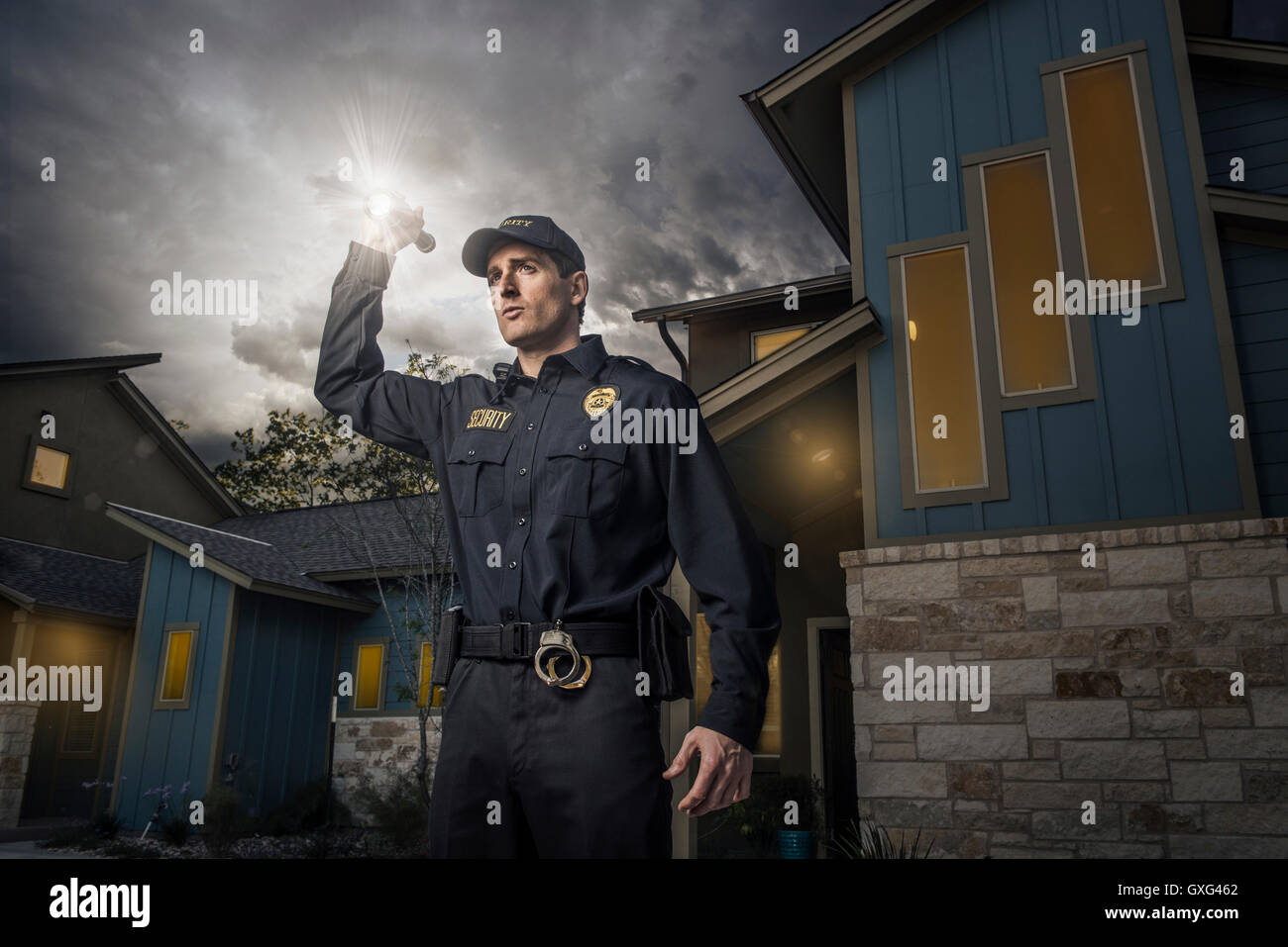 Caucasian police officer shining flashlight near house Stock Photo