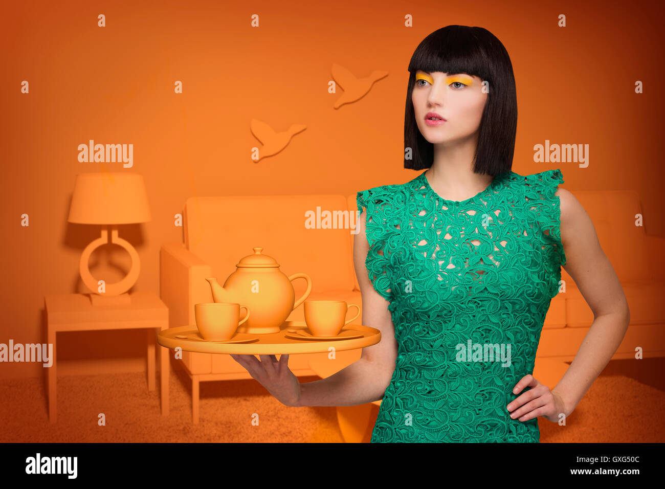 Caucasian woman in orange old-fashioned livingroom holding tea service Stock Photo