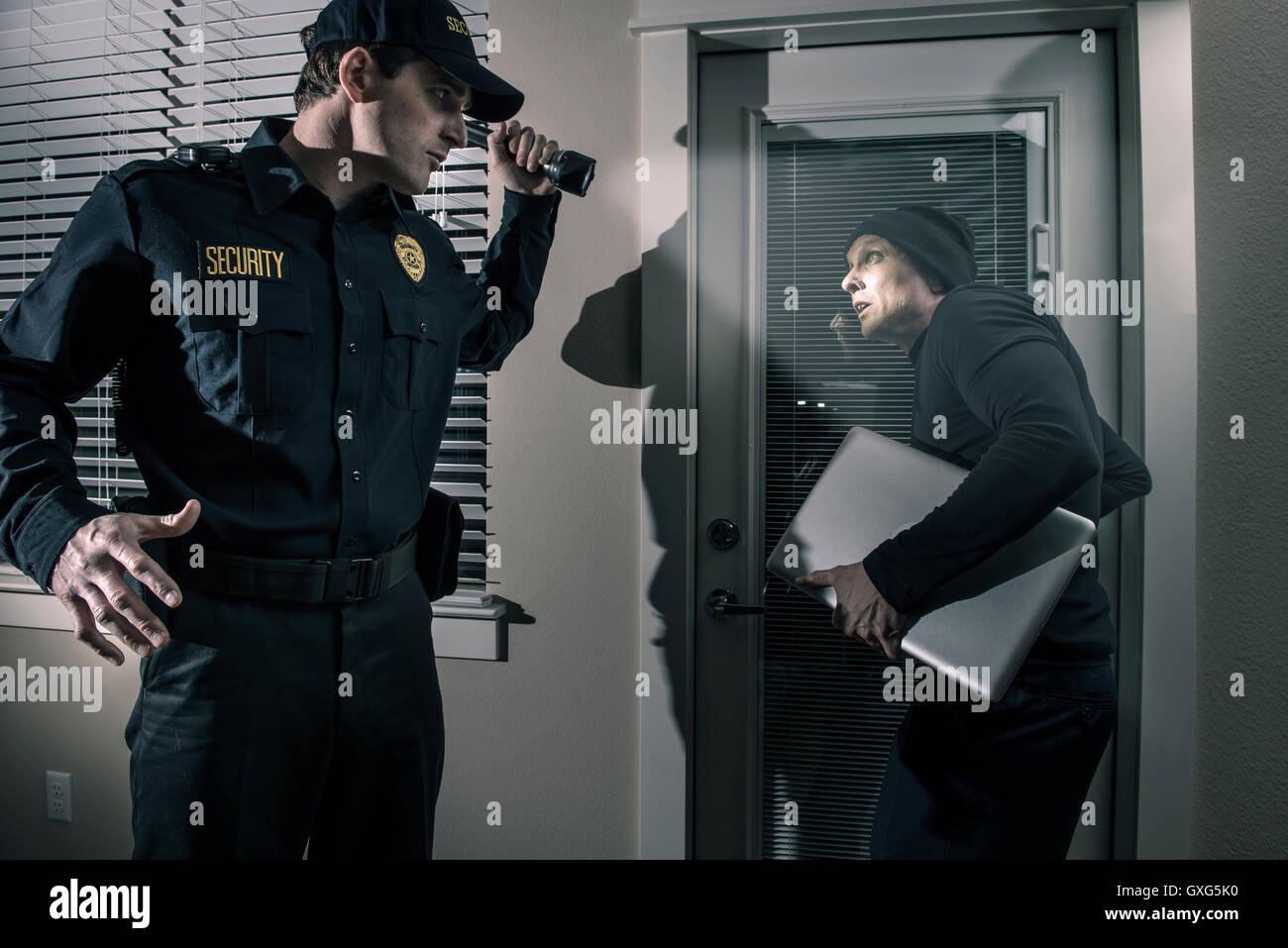 Caucasian police officer shining flashlight on burglar stealing laptop Stock Photo