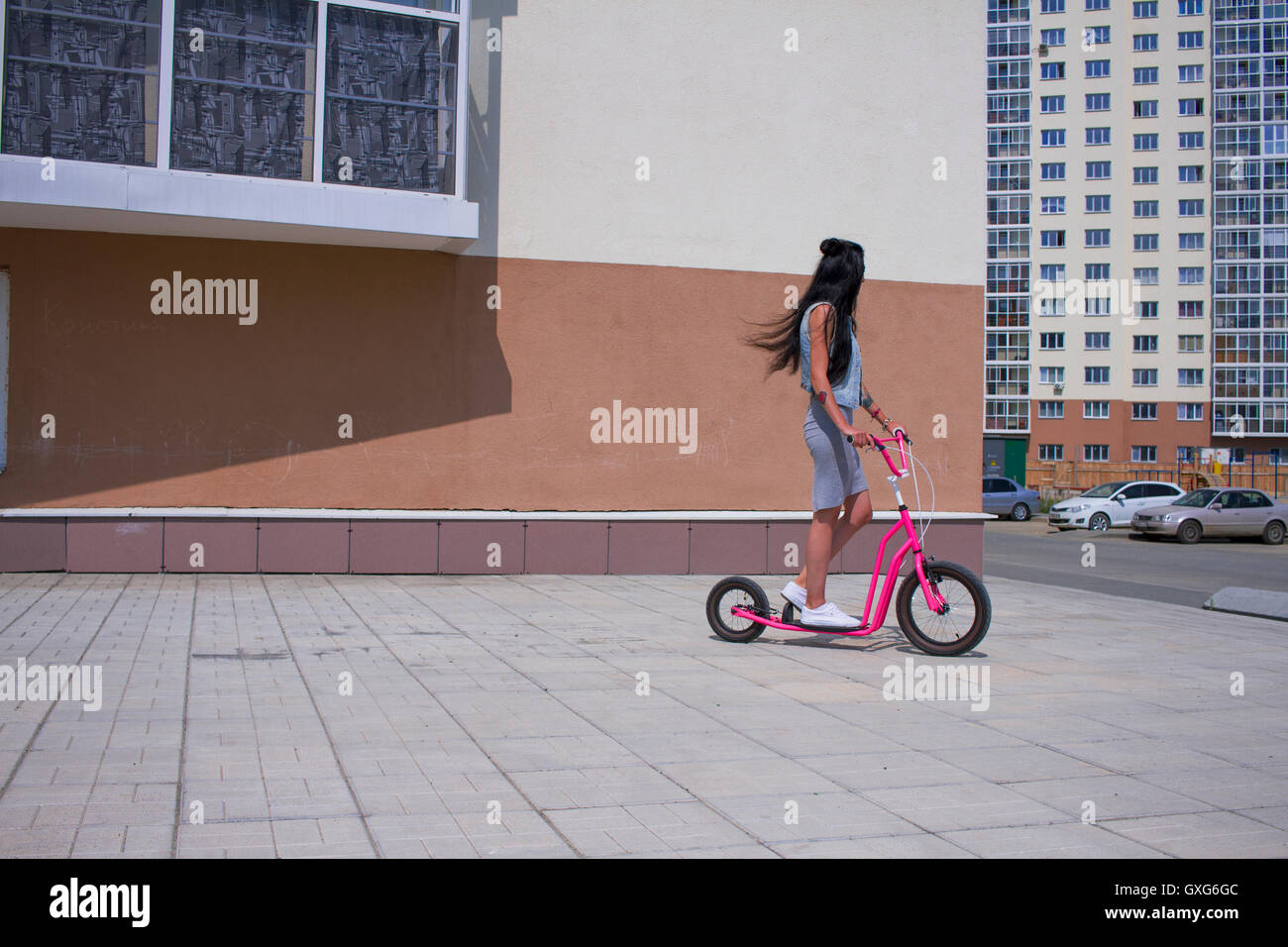 Caucasian woman riding push scooter on city sidewalk Stock Photo