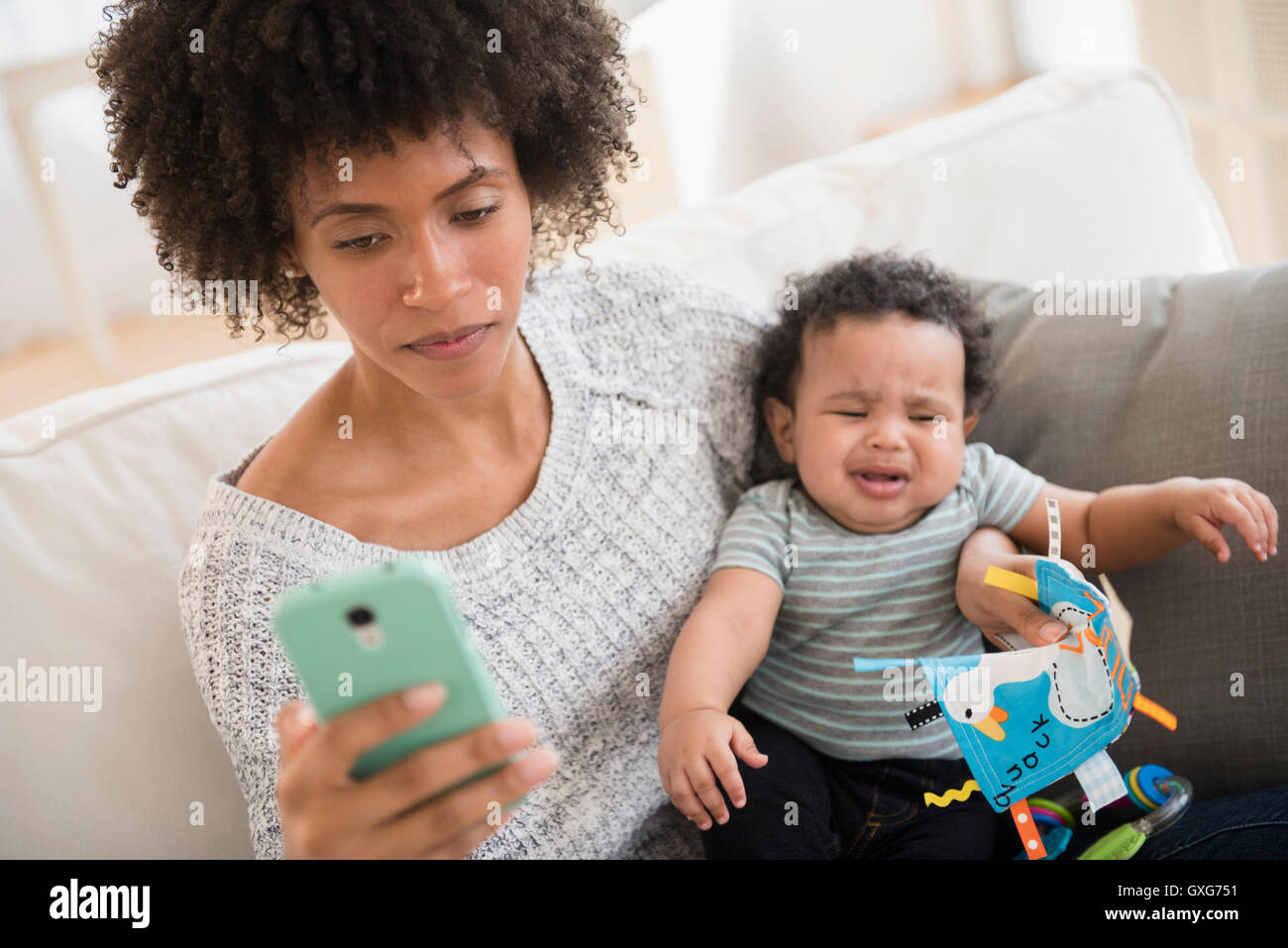 Mother holding crying baby son while texting on cell phone Stock Photo