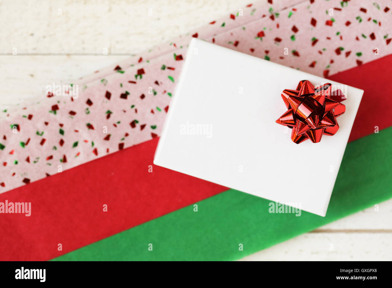 Small white gift box with red bow on colorful red and green tissue paper. Stock Photo