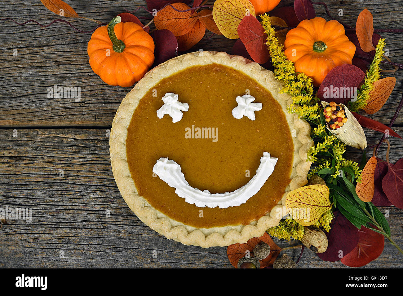 Autumn pumpkin pie with happy face in fall leaves on rustic wood Stock Photo