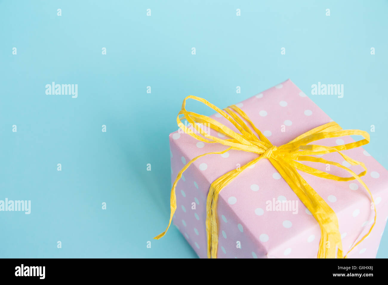 Top view of a gift box wrapped in pink dotted paper and tied yellow bow over light blue background. Stock Photo