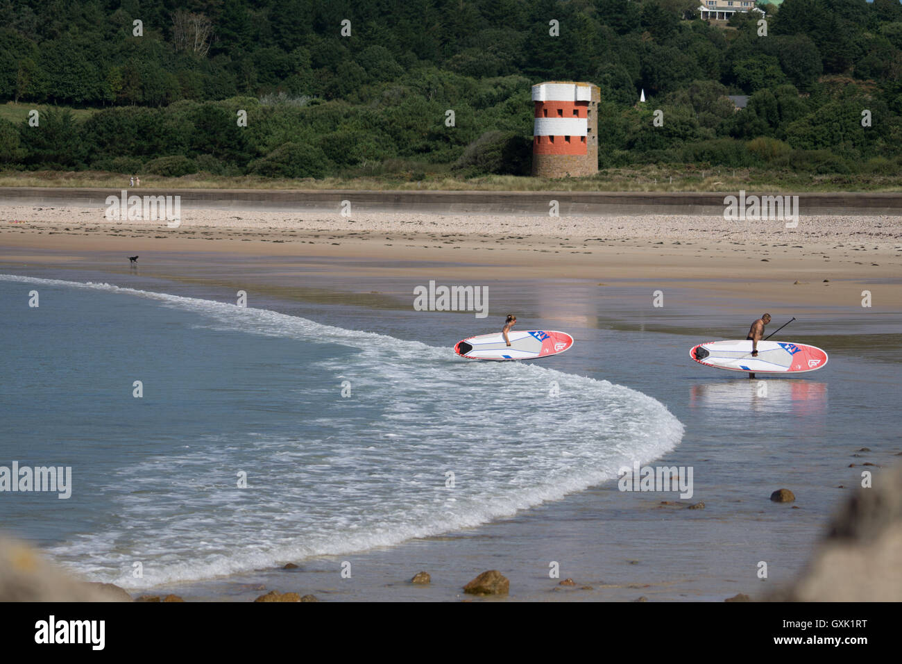 Paddle boarders exit the sea at Ouaisne Beach,St.Brelade,Jersey,Channel Islands. Stock Photo