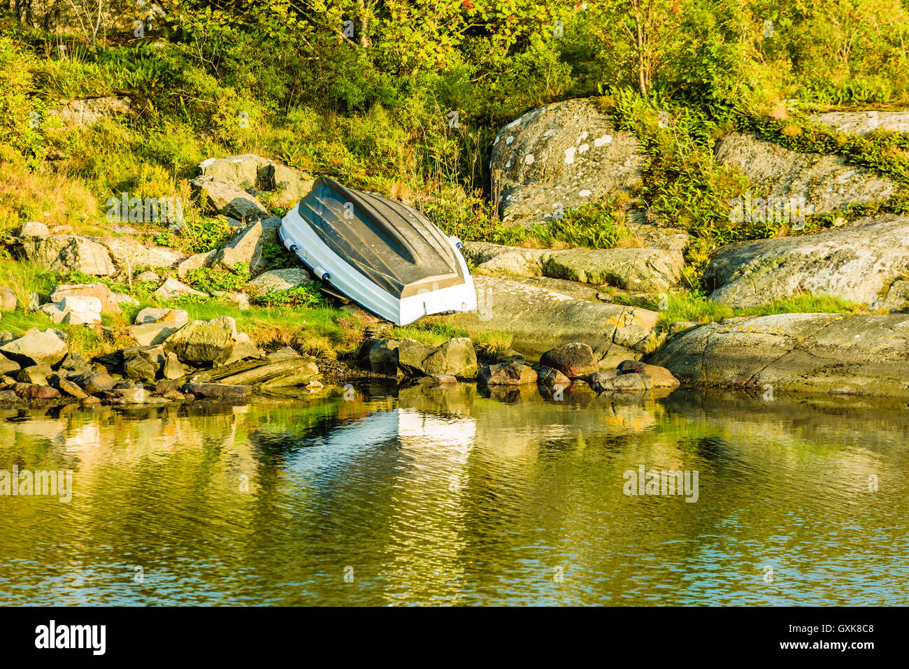 Upside down boat on the green shore and windless water in front. Stock Photo